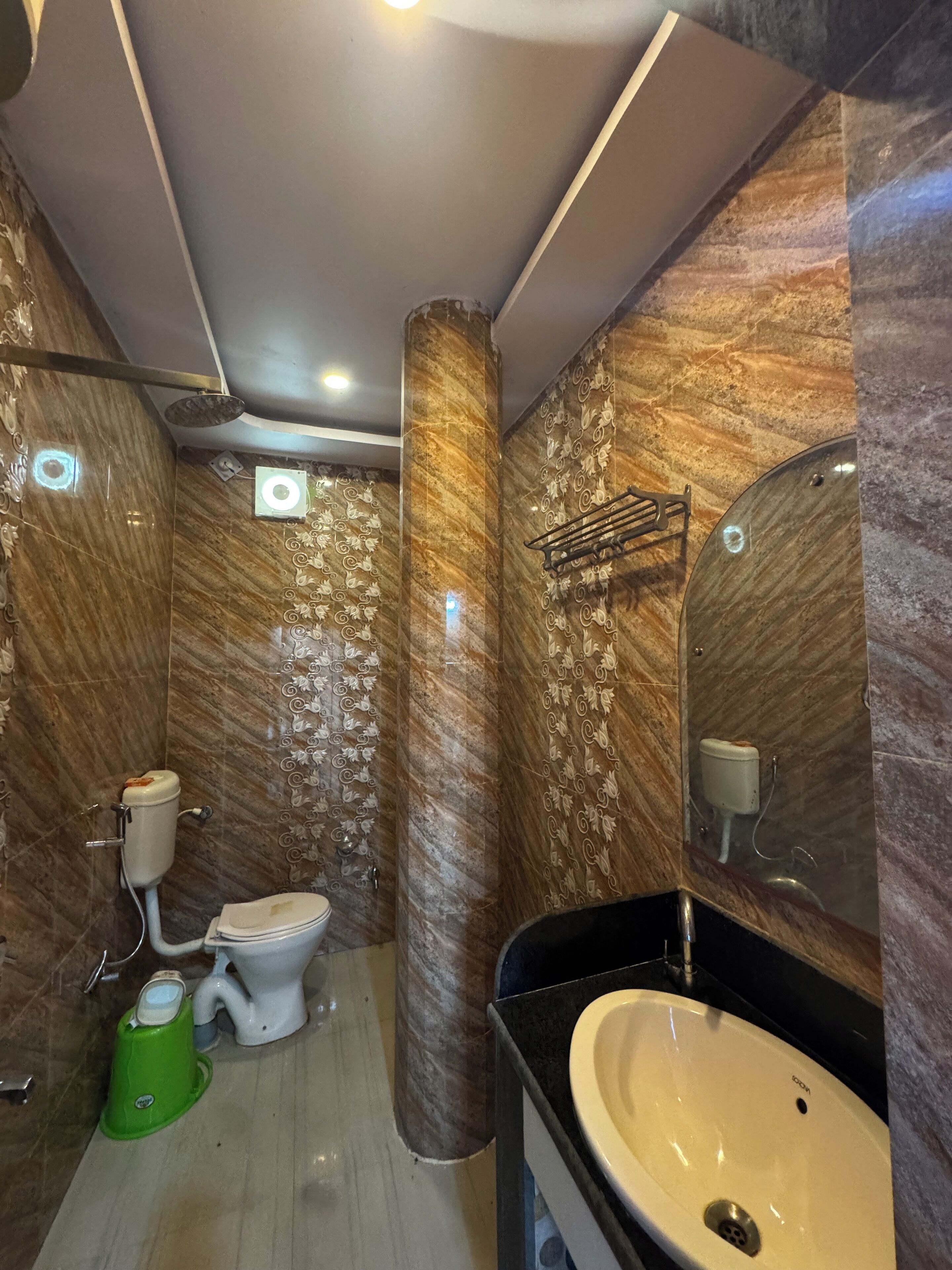 A modern bathroom with marble walls, a toilet, a sink, and a green trash bin.