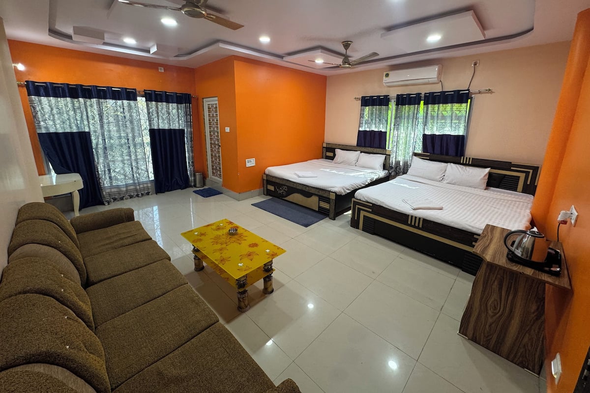 A hotel room with two beds, a sofa, a coffee table, and a ceiling fan.
