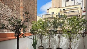 Eine Dachterrasse mit einer Ziegelwand, einem weißen Sofa mit Kissen und mehreren Kübelpflanzen.
