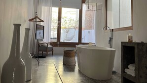 Ein modernes Badezimmer mit einer freistehenden Badewanne, einem großen Spiegel und einem Fenster mit Tageslicht.