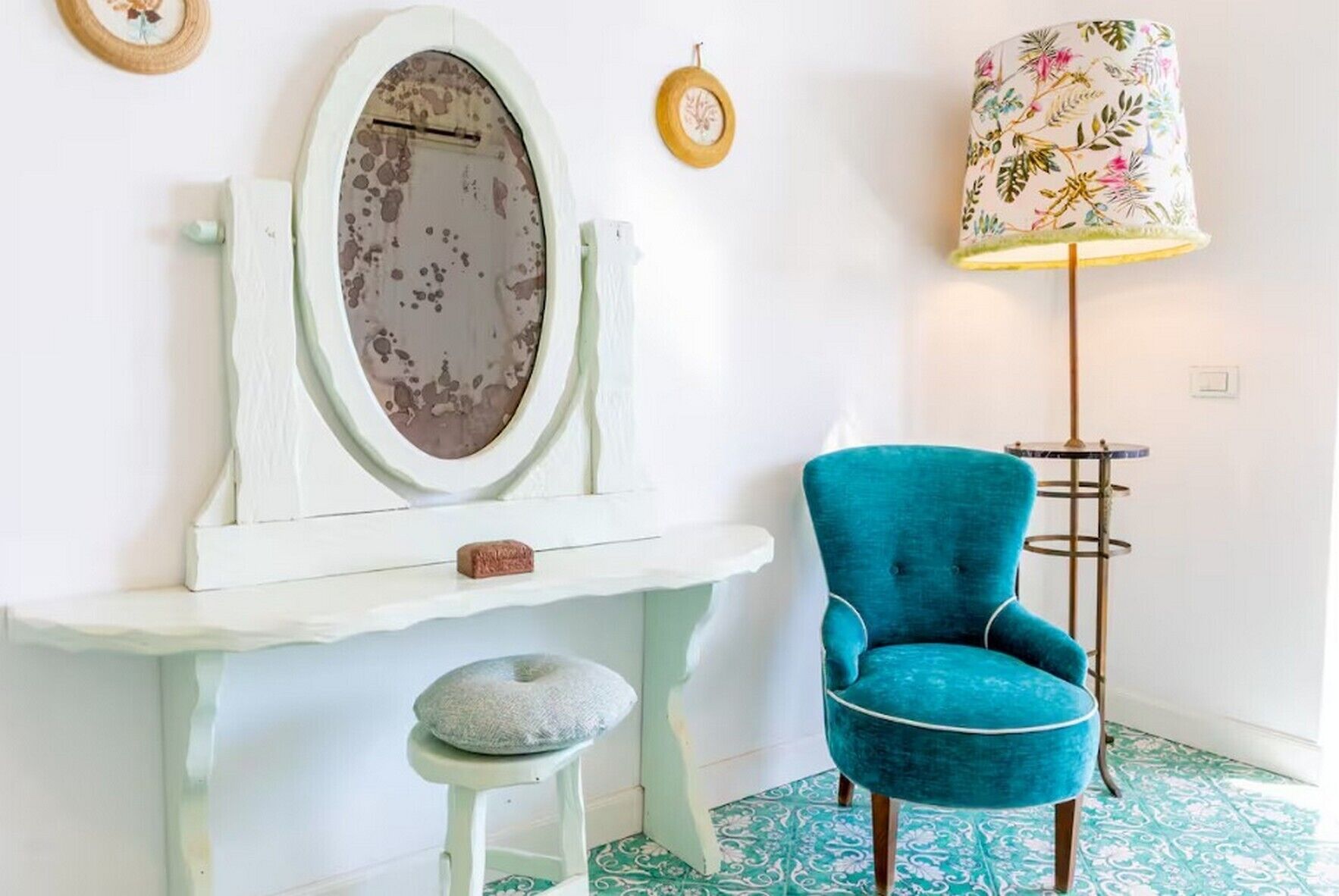 A room with a vanity, a blue armchair, a floor lamp, and patterned floor tiles.
