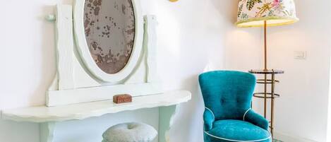 A room with a vanity, a blue armchair, a floor lamp, and patterned floor tiles.