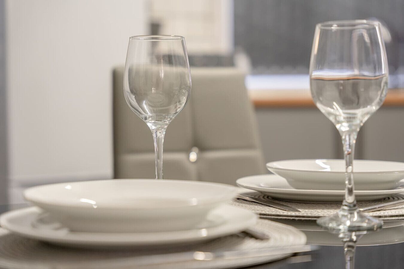 Een eettafel met witte borden en glazen wijnglazen, voor een neutrale achtergrond.
