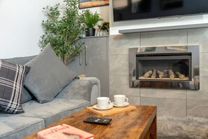A modern living room with a grey sofa, a coffee table, a fireplace, and a flat-screen TV mounted above it. - Two-bedroom home with games, fireplace and fast Wi-Fi (Lancashire)