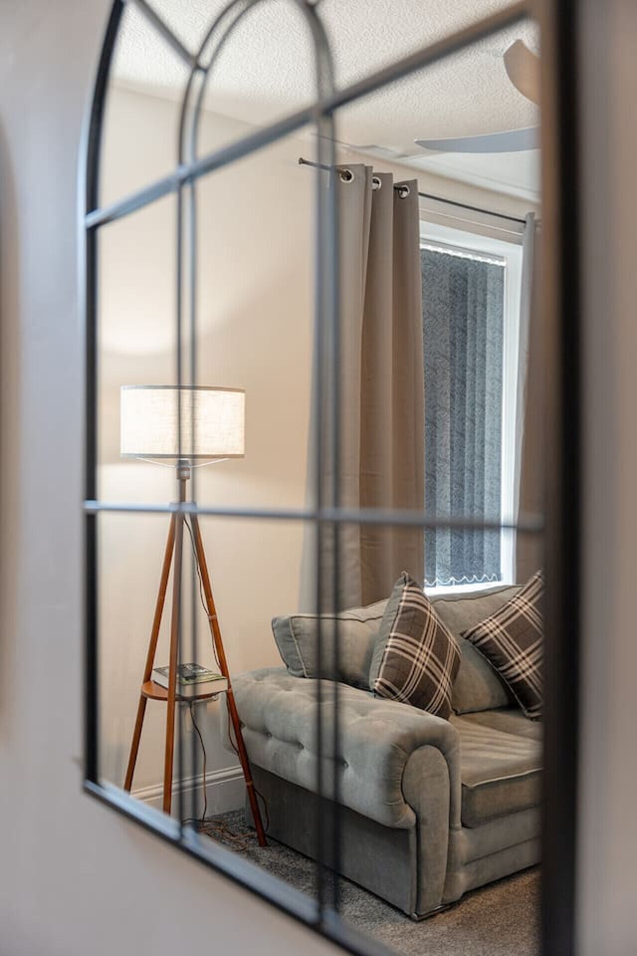Ein Zimmer mit grauem Sofa, einer Stehlampe und einem Fenster mit Vorhängen.