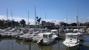 Un port esportiu amb diverses embarcacions amarrades, un edifici amb una bandera i un cel serè.