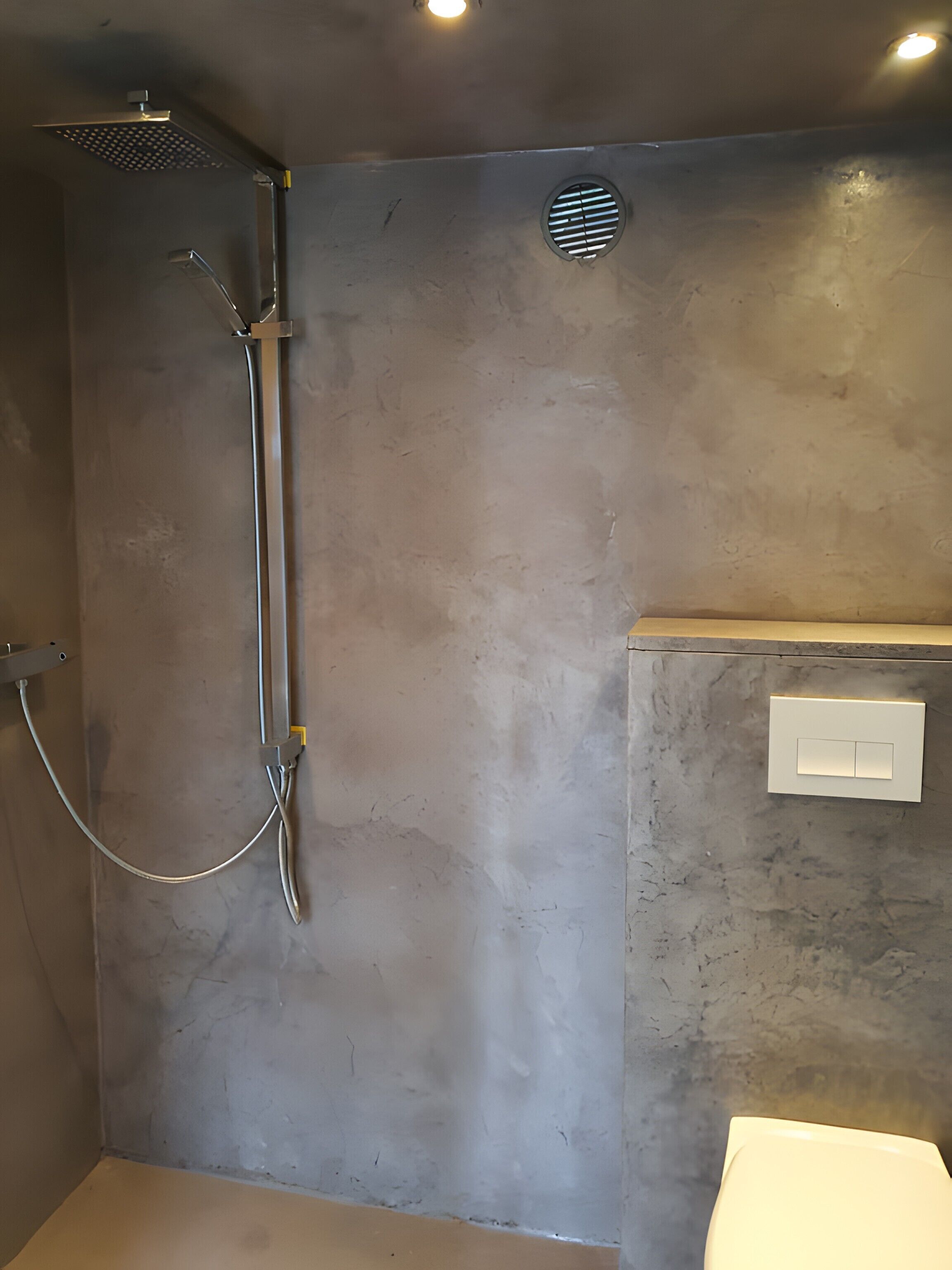 A bathroom with a shower, a toilet, and a light switch on the wall.