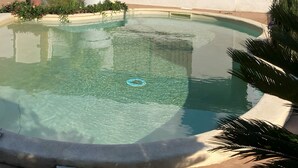 Una piscina transparent amb vora rodona, envoltada d'una terrassa de formigó i vegetació.