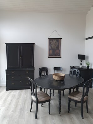 Un coin repas avec une table noire, quatre chaises, un buffet noir et un tableau encadré au mur.