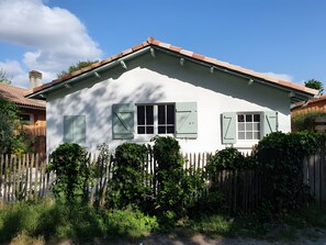 Une maison blanche aux volets verts, une clôture en bois et un ciel bleu azur.