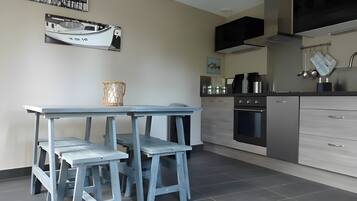 Een moderne keuken met een eethoek, met een tafel en krukken, een fornuis, oven en een spoelbak.