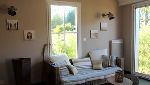 A wicker sofa with striped cushions, a small round table, and a window with a view of greenery.