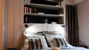 A bed with a fur throw, a hat, and a bookshelf above it.