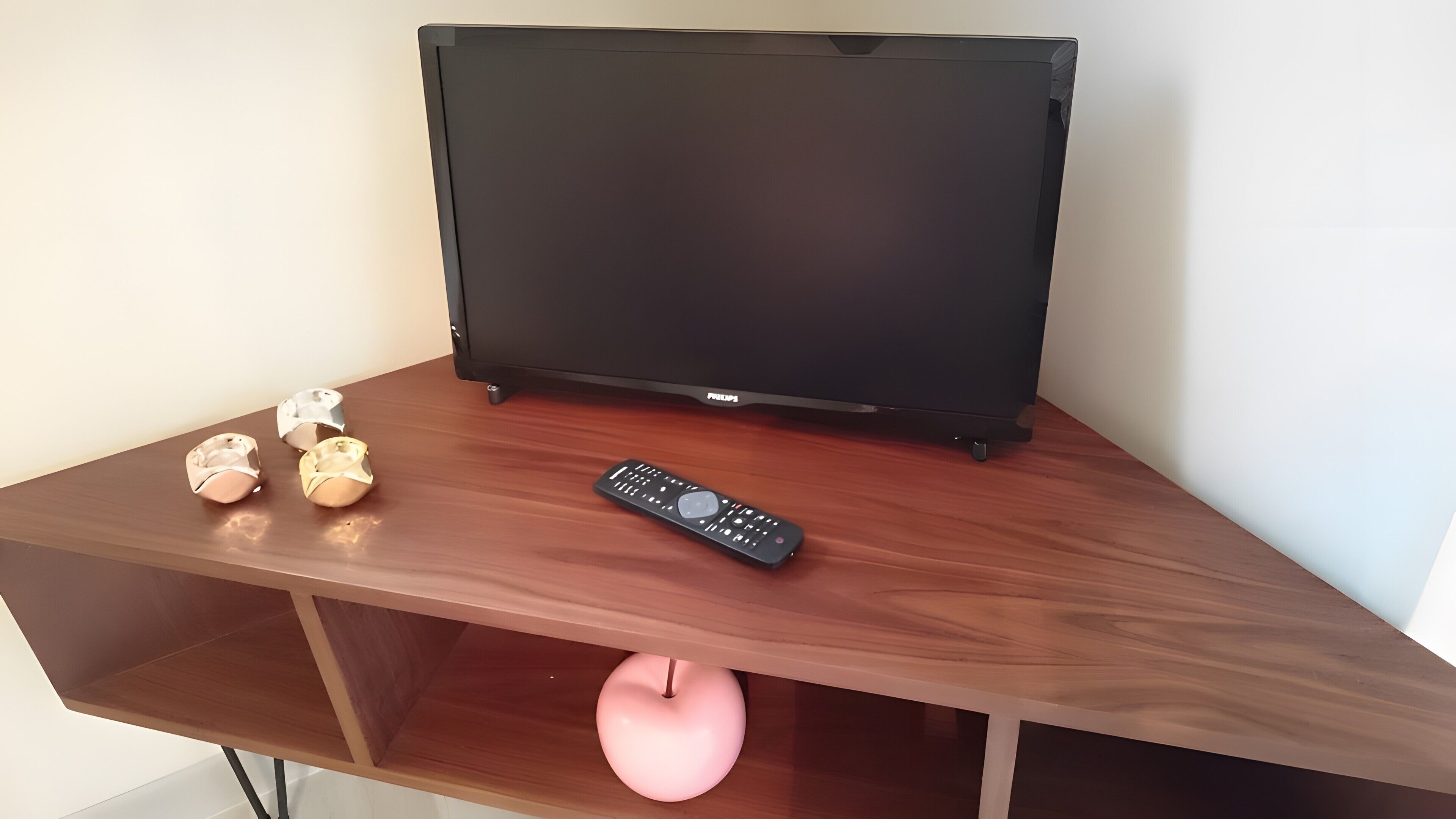 A wooden TV stand with a flat-screen TV, a remote control, and a pink apple.