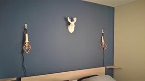 Une chambre avec un mur bleu foncé, une tête de lit en bois et deux lampes suspendues aux motifs géométriques.