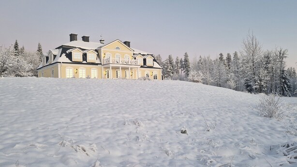 A large, two-story house with a symmetrical facade, surrounded by snow-covered trees and a snow-covered lawn.