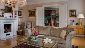 A living room with a fireplace, a chandelier, a sofa, a coffee table, and a dining area visible through an open door.