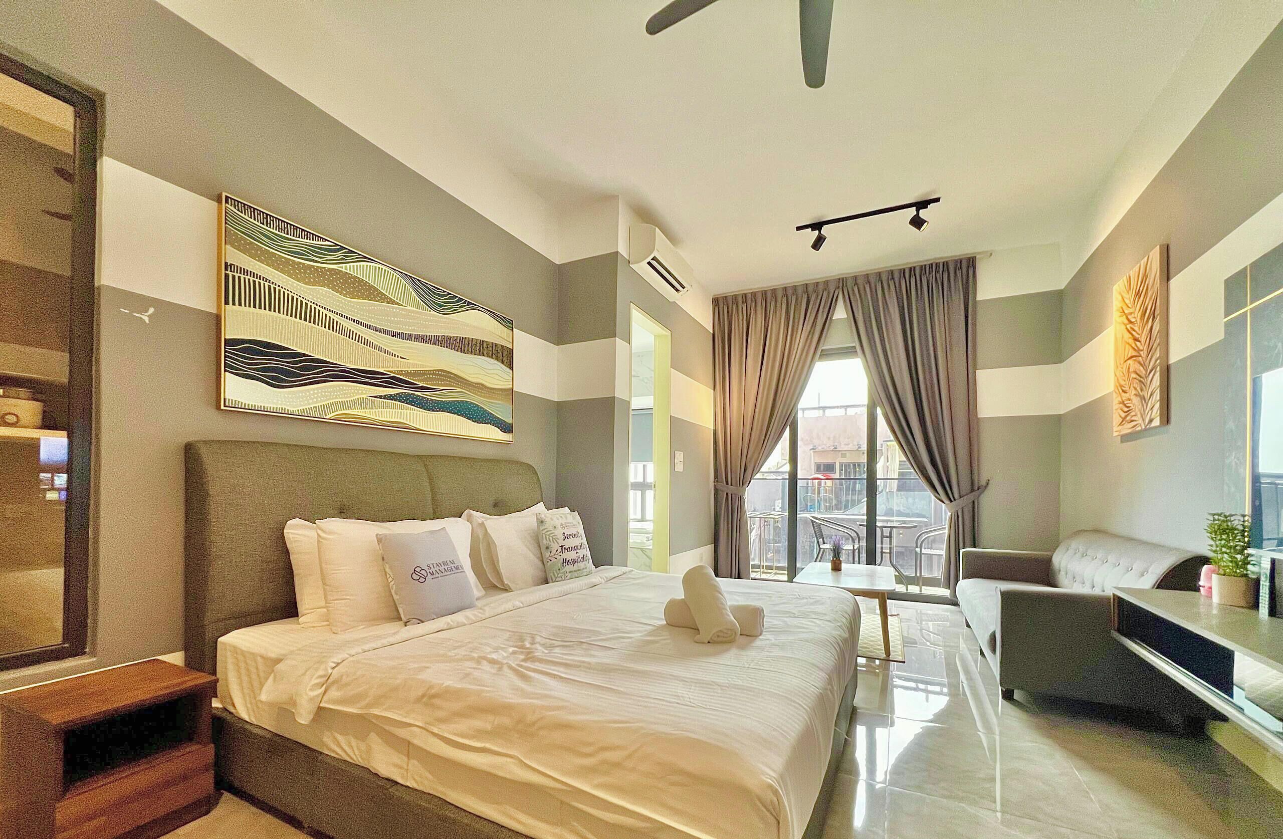 A modern hotel room with a large bed, a sofa, a desk, and a view of the city through large windows.
