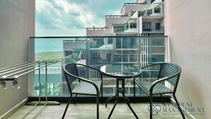 A balcony with a glass railing, two wicker chairs, and a small round table. - Imperio Residence Melaka by Stayrene (Malacca City)
