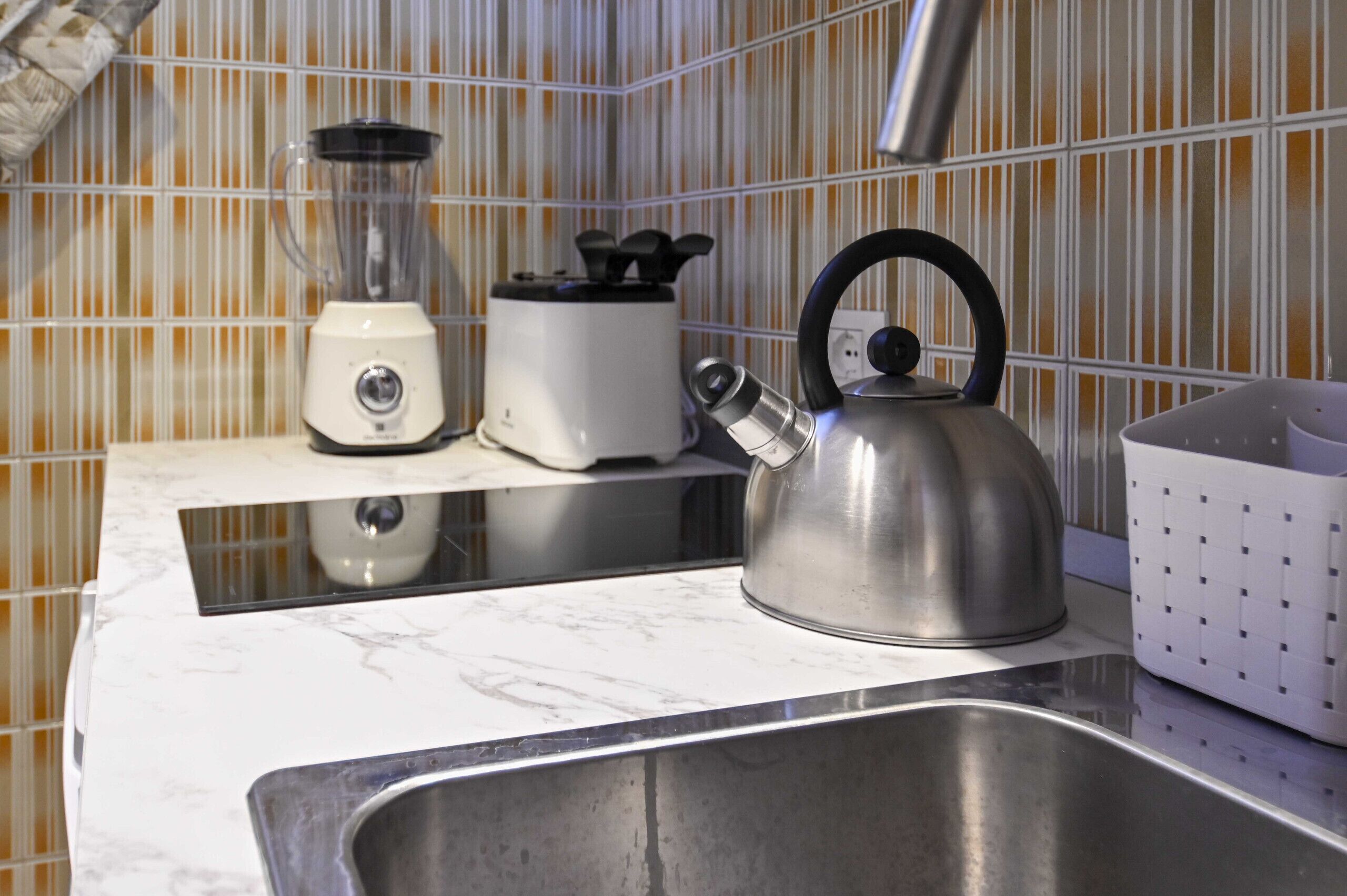 A kitchen with a stainless steel kettle, a blender, and a toaster on a marble countertop.