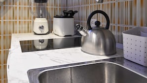 Ett kök med en vattenkokare i rostfritt stål, en mixer och en brödrost placerade på en bänkskiva i marmor.