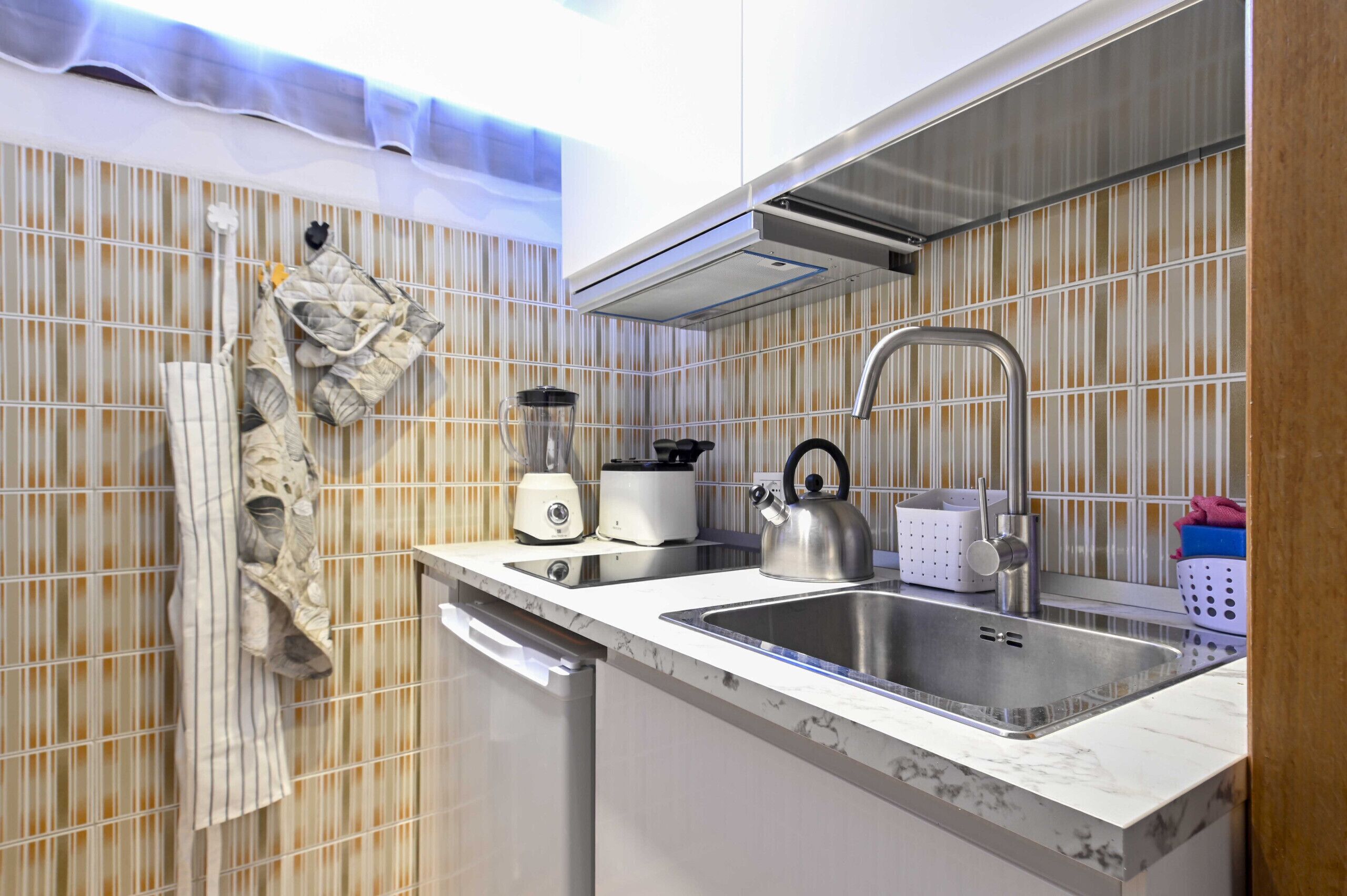 A modern kitchen with a stainless steel sink, a kettle, a toaster, and a blender.