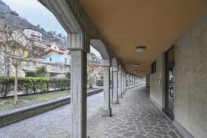 A covered walkway with stone flooring, supported by columns, leading to a building entrance. - Casa Angolo (Angolo Terme)