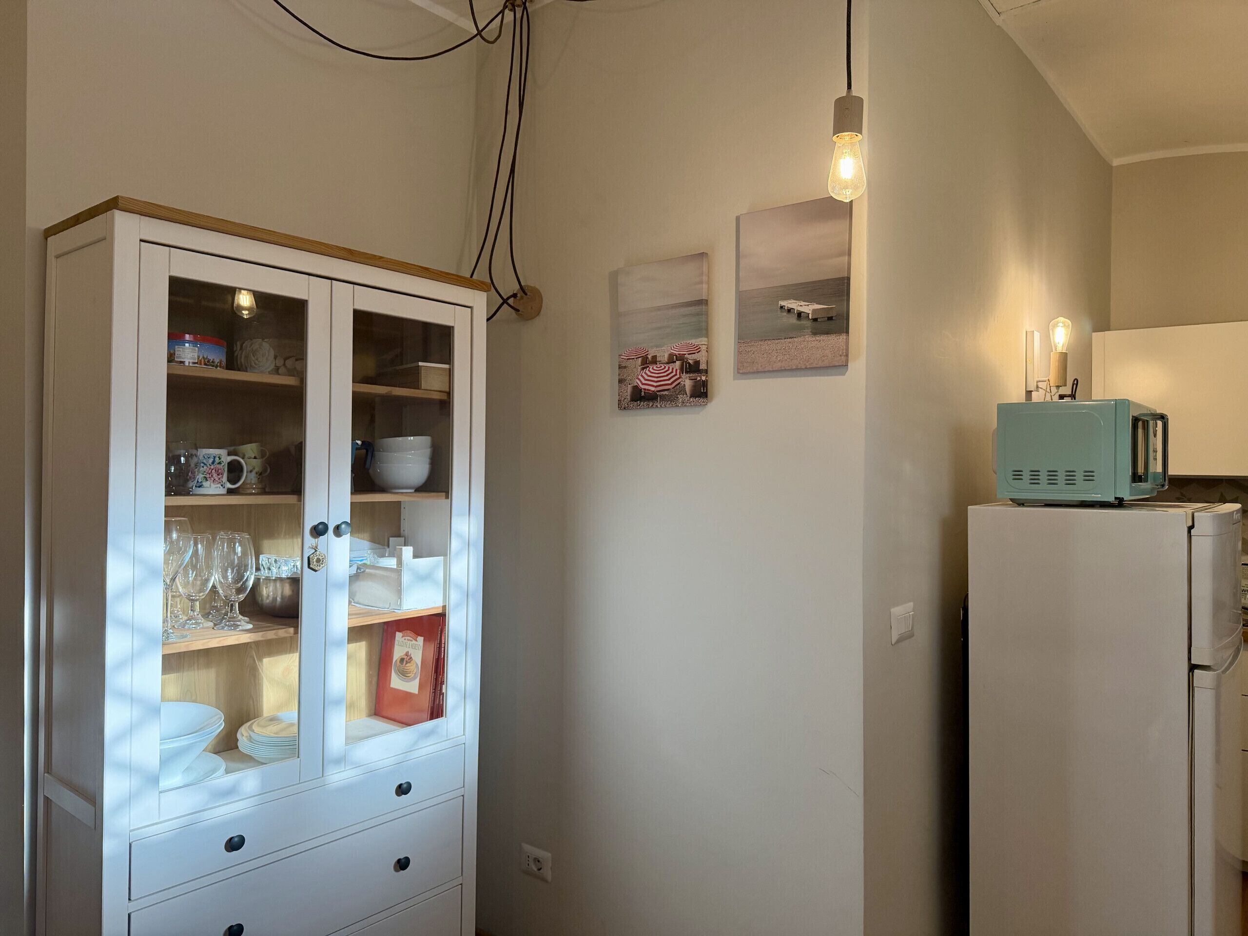 Una cucina con un armadietto bianco, un forno a microonde color acquamarina in stile retrò e un portalampada fissato al muro.