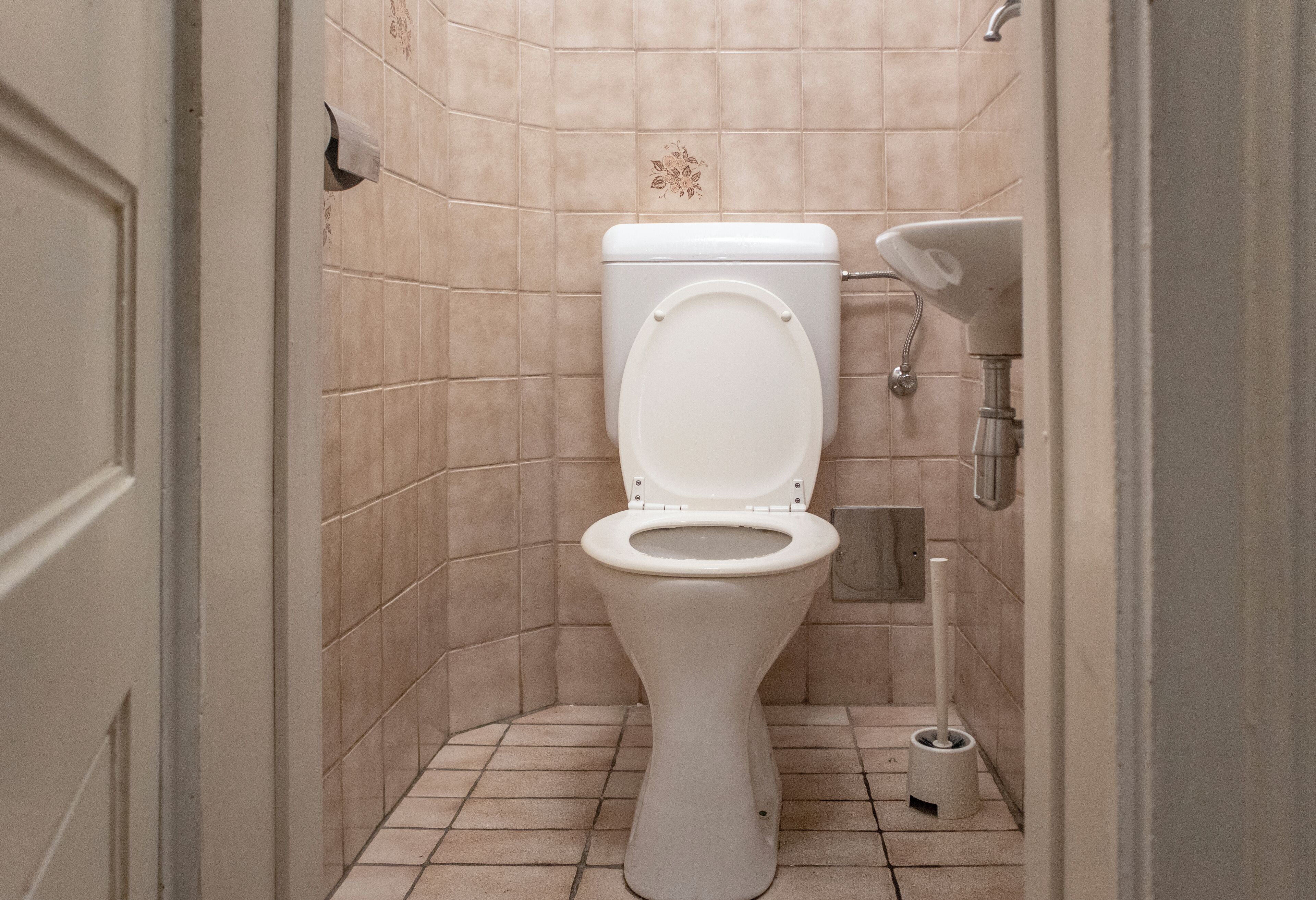 Ein kleines Badezimmer mit Fliesen, Toilette, Waschbecken und WC-Bürste.