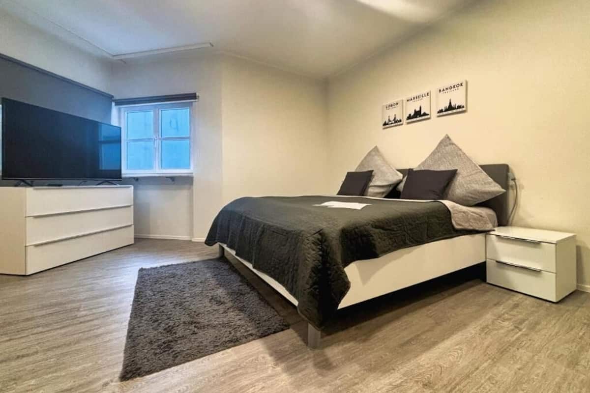 Ein Schlafzimmer mit Bett, Nachttisch, Kommode, Flachbildfernseher und Fenster.