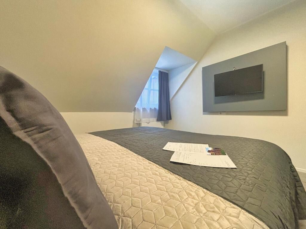 A bedroom with a bed, a TV mounted on the wall, and a window with a curtain.