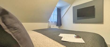 Un dormitorio con una cama, un televisor montado en la pared y una ventana con cortina.