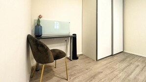 Ein Zimmer mit Schreibtisch, Stuhl, weißem Schrank und einer kleinen Topfpflanze.