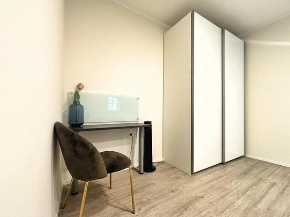Quarto com escrivaninha, cadeira, guarda-roupa branco e uma pequena planta em vaso.