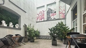 Ein Innenhof mit Fliesenböden, Sitzgelegenheiten im Freien und einem Wandgemälde mit Tieren.