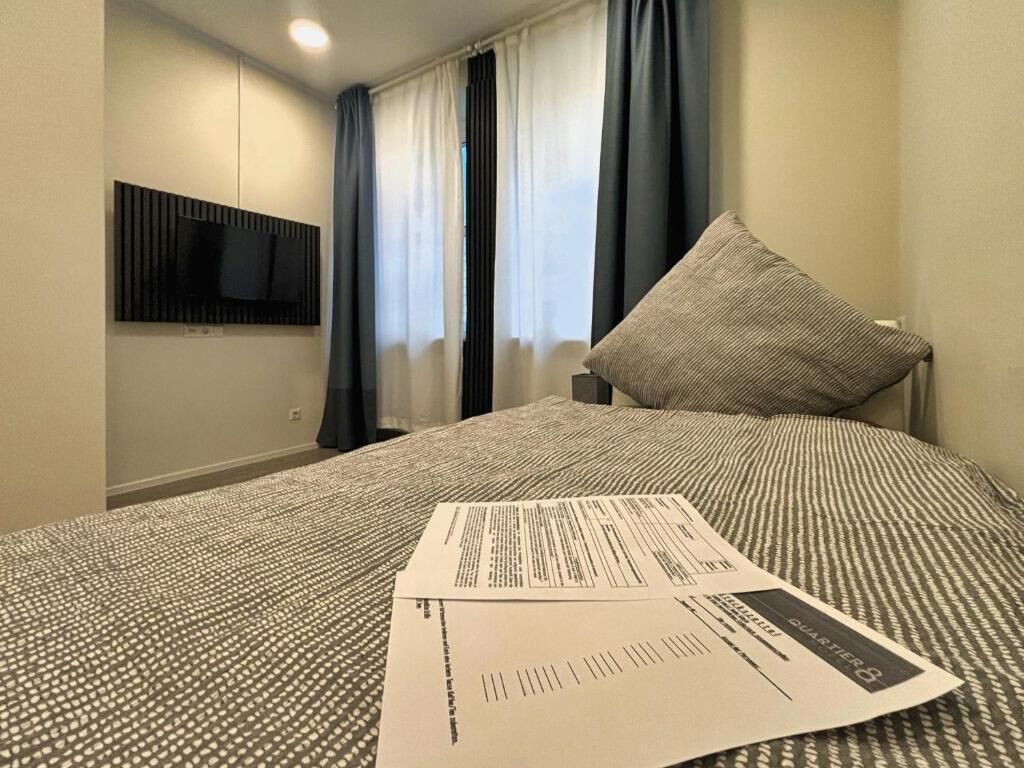Habitación de hotel con cama, televisor de pantalla plana en la pared y ventana con cortinas.