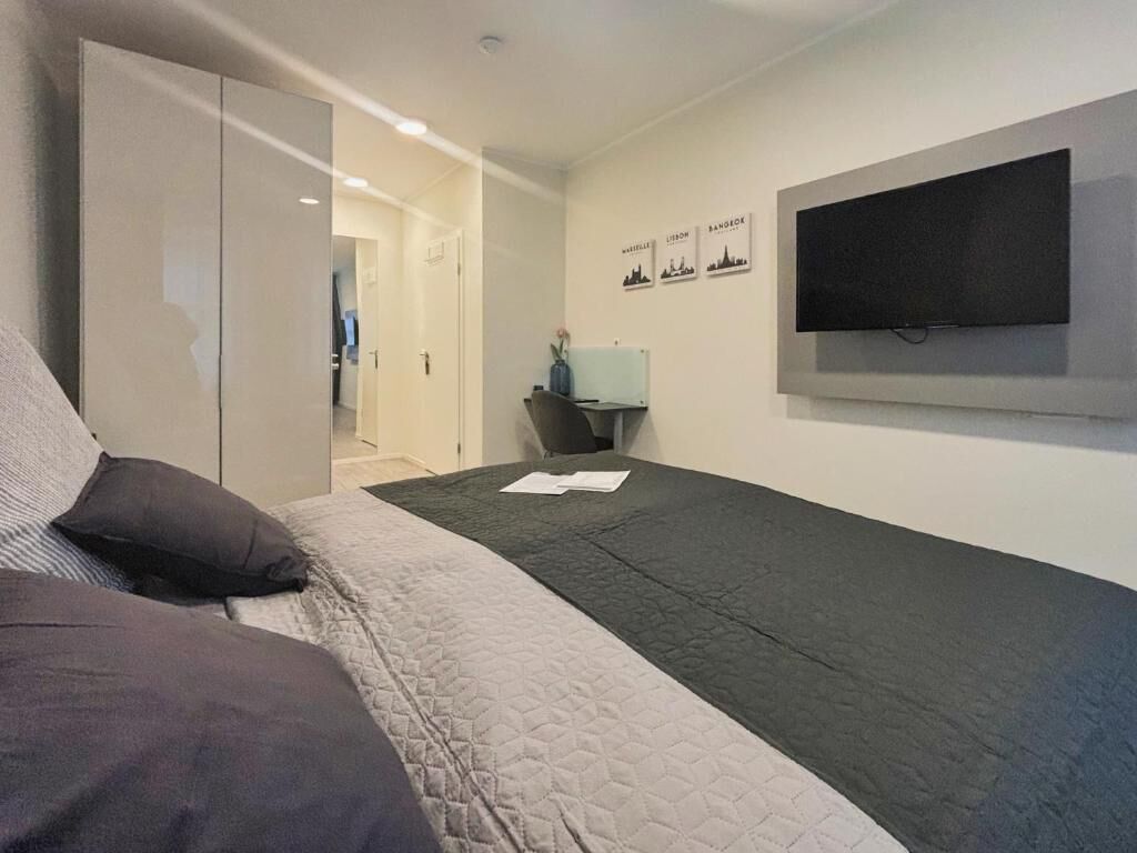 Un dormitorio con cama, televisor montado en la pared y escritorio con silla.