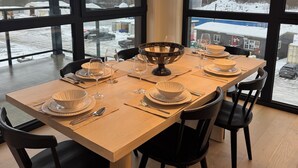A dining table set for six with black chairs, a large window with a view of a snowy landscape, and a hanging pendant light. - Spacious corner retreat with panoramic mountain views, floor-to-ceiling windows, and designer interiors—minutes from Revelstoke Mountain Resort and downtown. (Revelstoke)