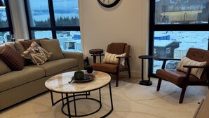 A living room with a large window, a round table, a sofa, and a chair. - Spacious corner retreat with panoramic mountain views, floor-to-ceiling windows, and designer interiors—minutes from Revelstoke Mountain Resort and downtown. (Revelstoke)