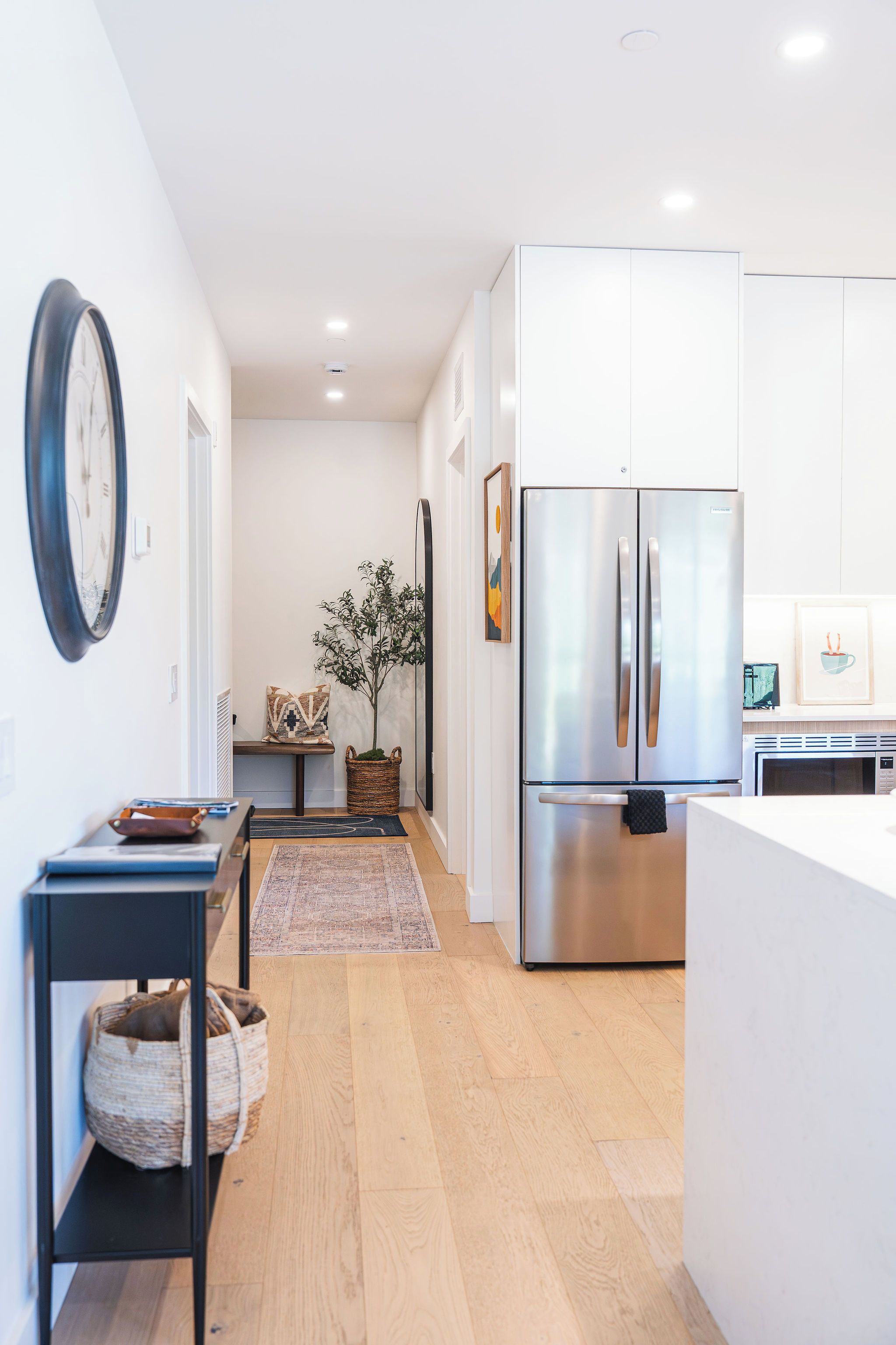 A modern kitchen with white cabinets, a stainless steel refrigerator, and a wooden floor.