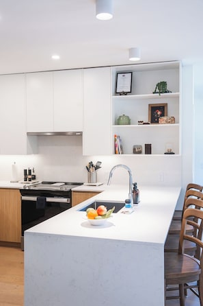 Een moderne keuken met witte kasten, een centraal keukenblok met een spoelbak en een inbouwkast.