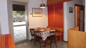 Zona pranzo con tavolo imbandito per quattro persone, sedie in legno, lampadario a sospensione e un quadro appeso alla parete.