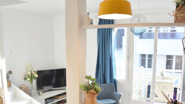 Ein modernes Wohnzimmer mit einem gebogenen Couchtisch aus Holz, einem blauen Sessel, einem Fernseher und einer gelben Pendelleuchte.