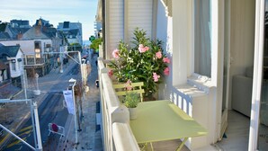 Ein Balkon mit Tisch und Kübelpflanzen, mit Blick auf eine Straße mit Häusern.
