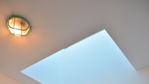 Ein Schlafzimmer mit Dachfenster, einem runden Spiegel an der Wand und einem Bett mit gestreifter Bettdecke.