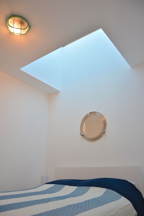 A bedroom with a skylight, a round mirror on the wall, and a bed with a striped bedspread.