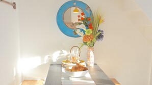 Ein Esstisch mit schwarzer Tischplatte, hölzernen Bänken, einer weißen Lampe, einem runden Spiegel und einer Blumenvase.