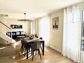A dining area with a table, chairs, and a fruit bowl. There is a staircase leading to another room, a sofa, and a painting on the wall. - Villa Amaryves à La Baule (La Baule-Escoublac)