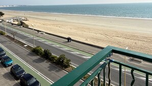 A coastal road with a beach in the background, a clear sky, and parked cars along the side. - Face mer à La Baule : Le Neptune (La Baule-Escoublac)