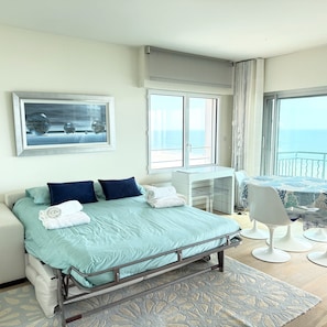 Habitación de hotel con cama, escritorio, silla y un amplio ventanal con vista al mar.